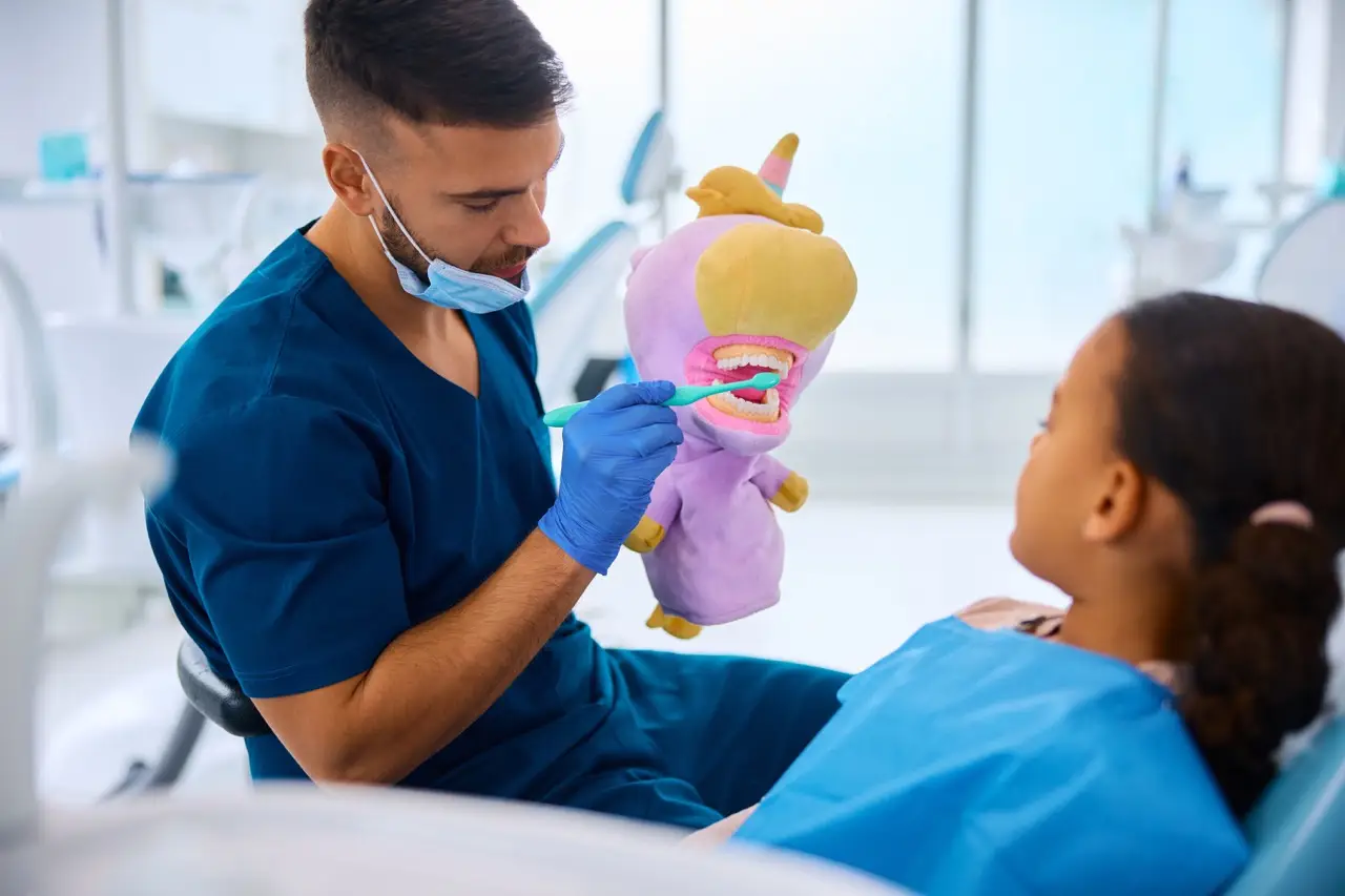 Dentist teaching black little girl to wash her teeth properly during appointment at dental clinic.