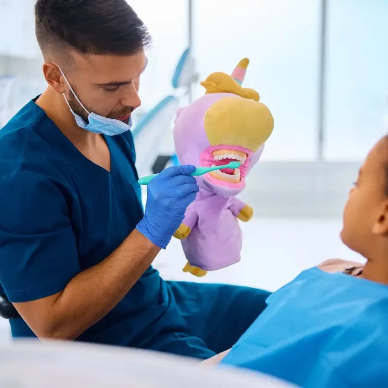 Dentist teaching black little girl to wash her teeth properly during appointment at dental clinic.
